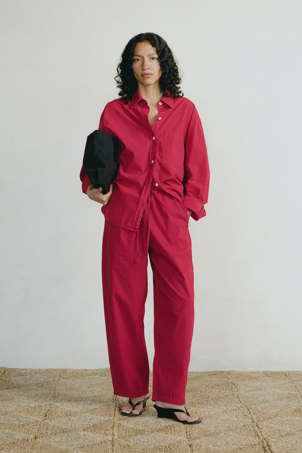 Woman wearing a red outfit holding a black bag against a white background