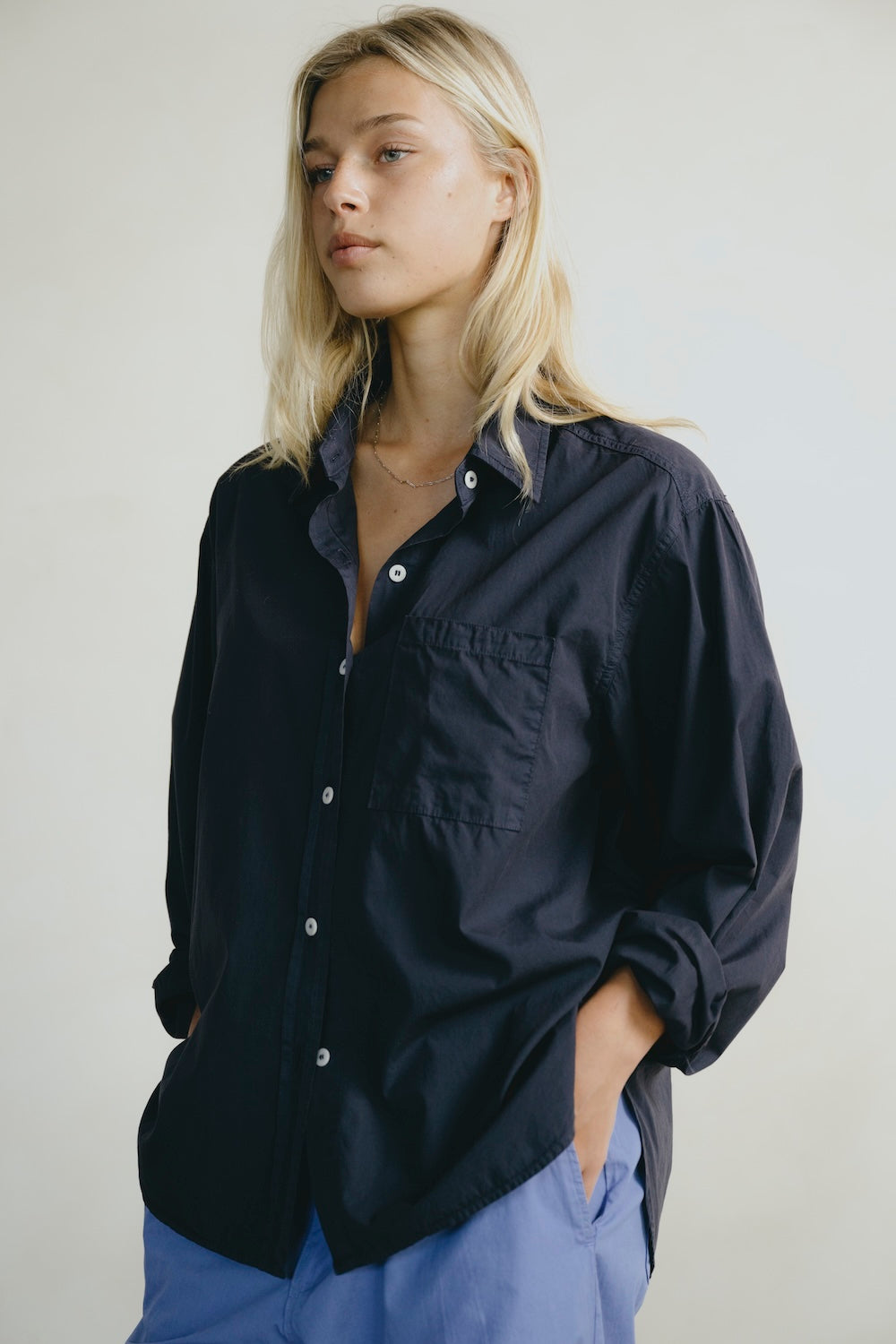 Woman wearing a dark blue shirt with rolled-up sleeves against a plain background