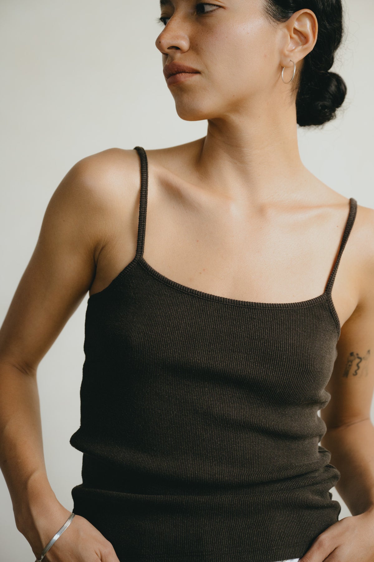 A woman wearing a dark brown ribbed knit camisole top with thin spaghetti straps, shown from the chest up against a plain light background.