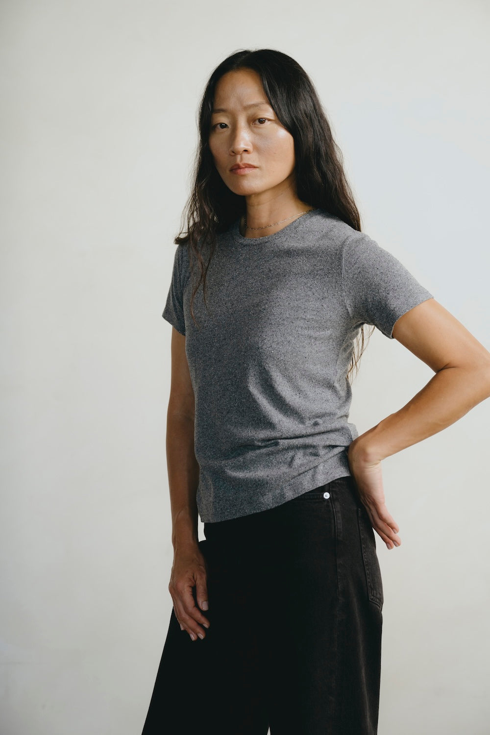 Woman wearing a gray t-shirt and black pants against a plain background