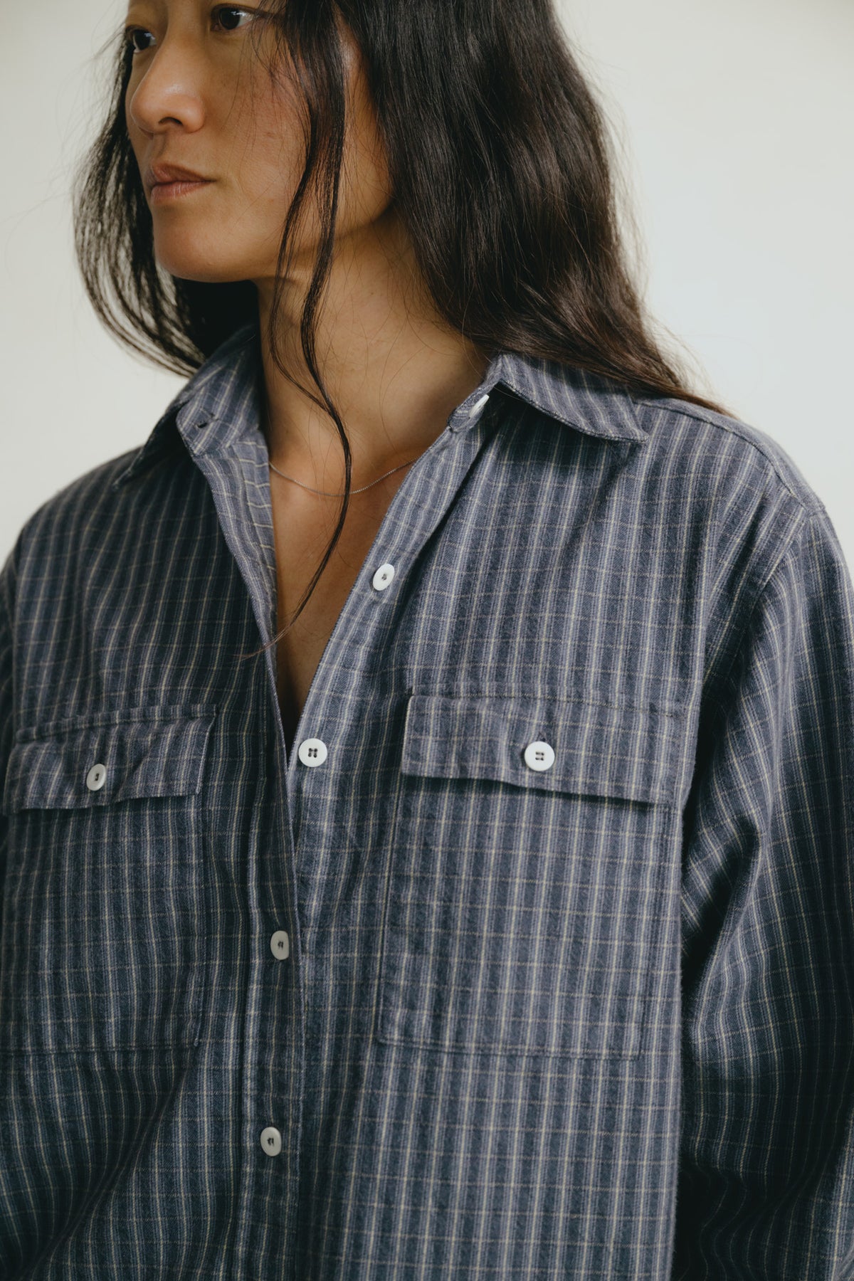 A close-up of a person wearing a dark blue-gray and white vertically striped button-up shirt with two chest pockets and white buttons.