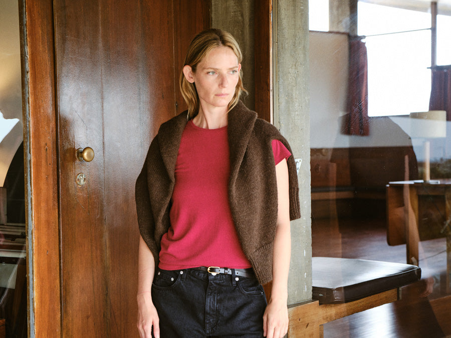 A woman standing against a wood doorway in a red crewneck tshirt.