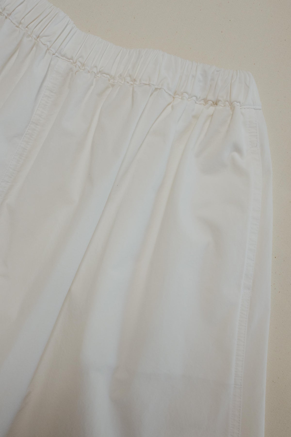 A close-up of white fabric with an elastic waistband, photographed against a plain light beige background.