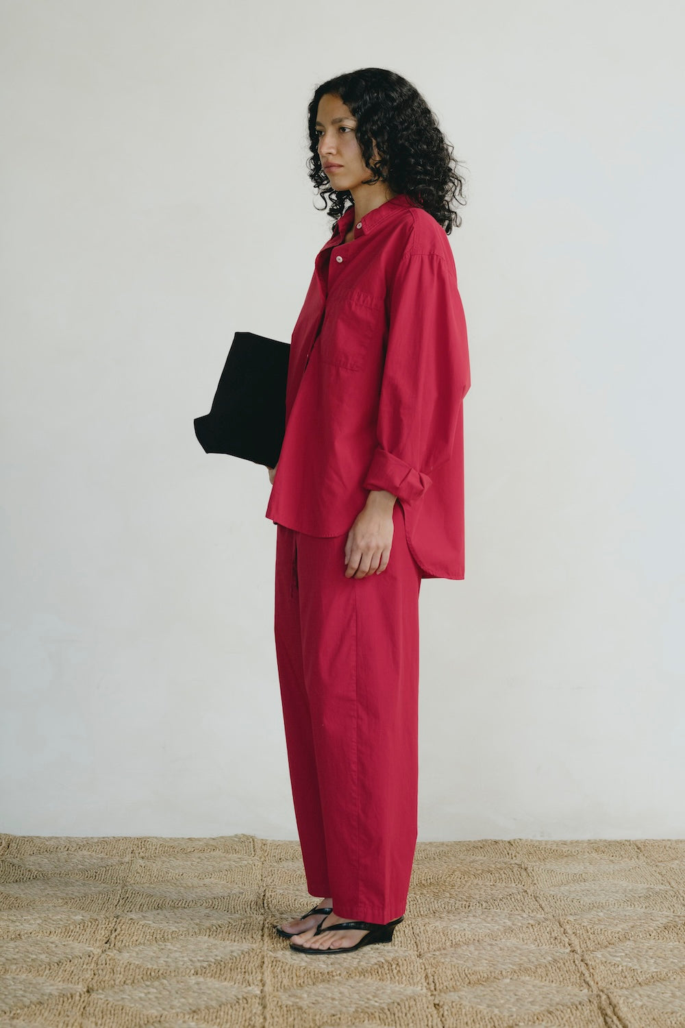 Woman in a red outfit holding a black bag on a textured floor with a white wall background