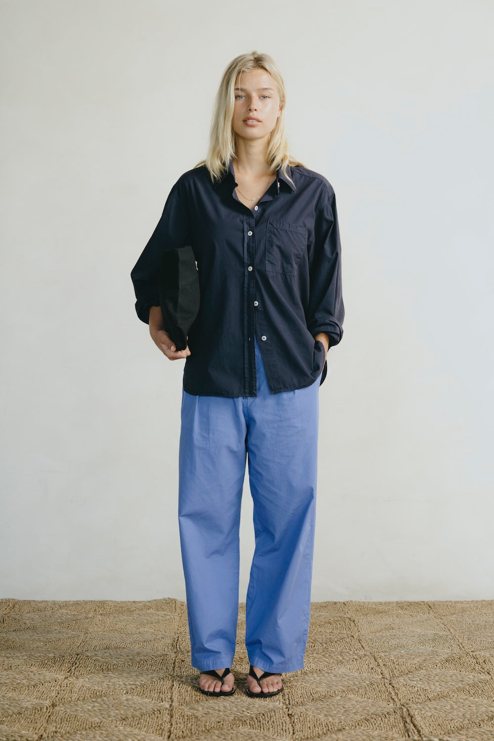 Person wearing a dark shirt and blue pants standing against a plain background