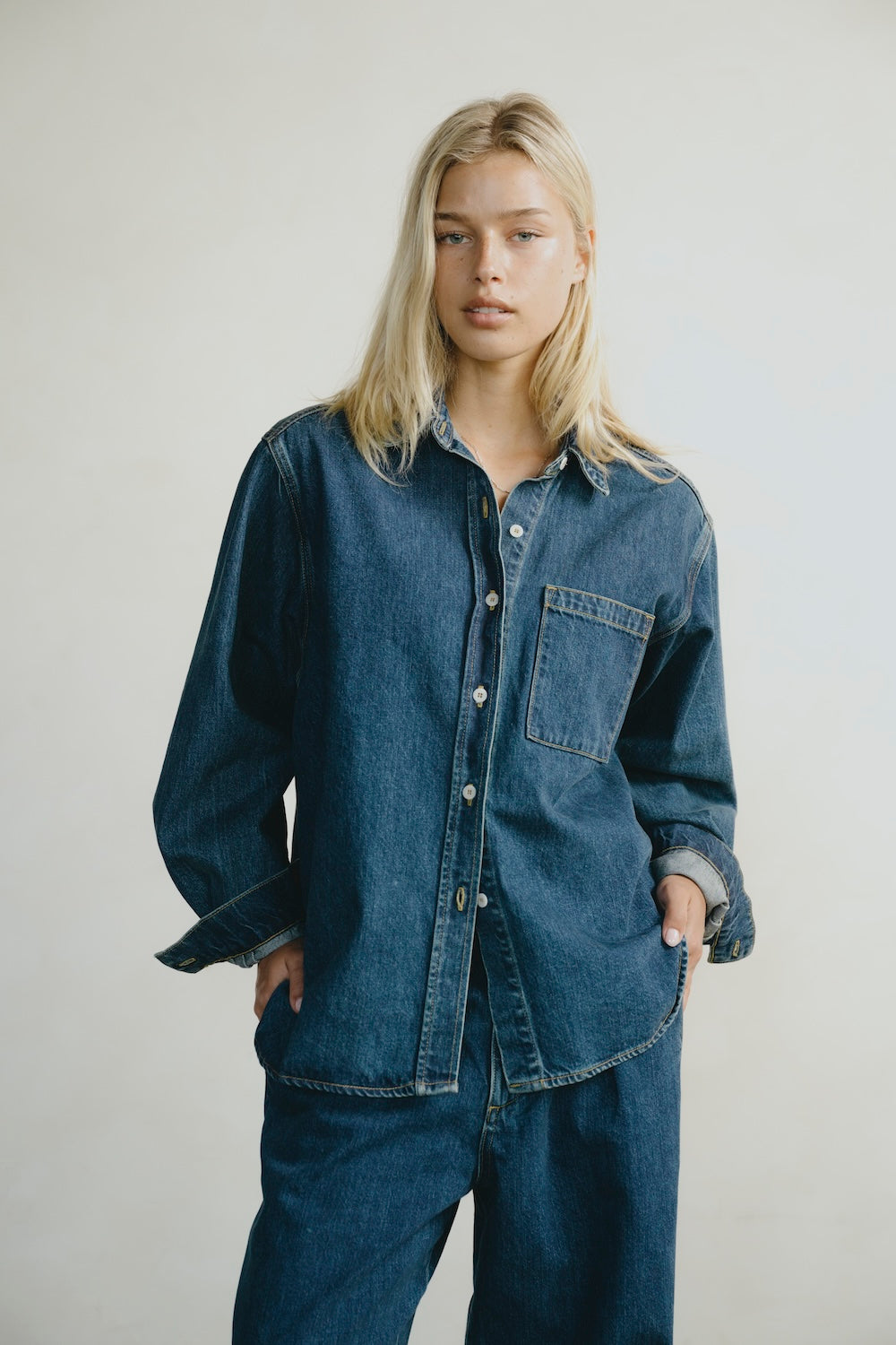 Person wearing a blue denim shirt and pants against a plain background