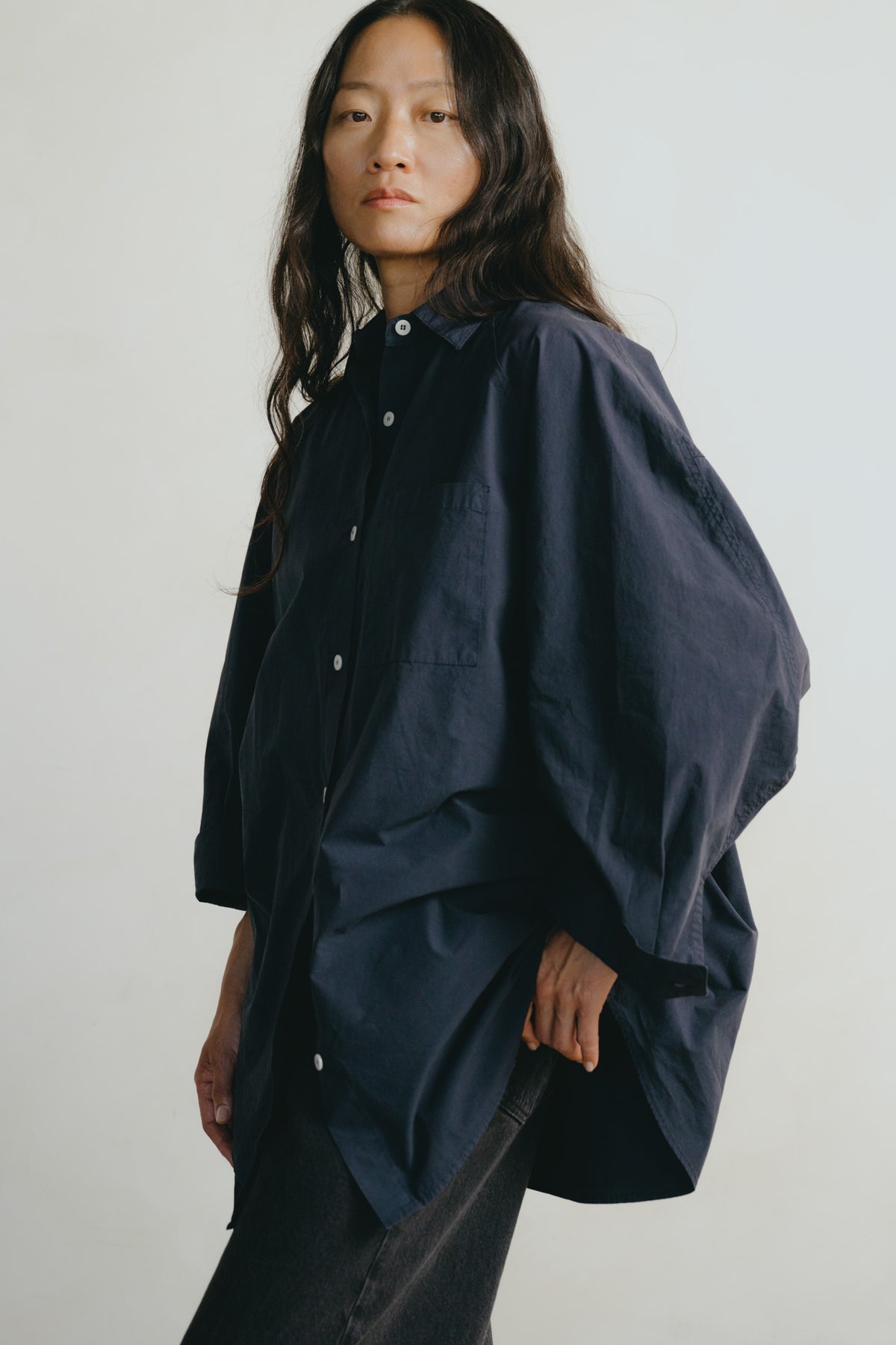 A model wearing an oversized dark navy blue button-up shirt with voluminous sleeves, photographed against a plain light gray background.