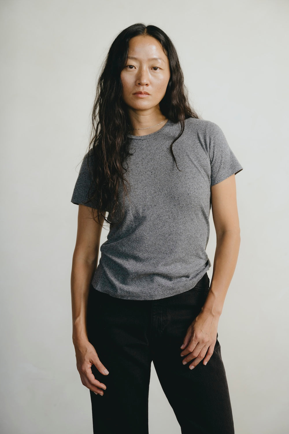 Person wearing a gray t-shirt and black pants against a plain background