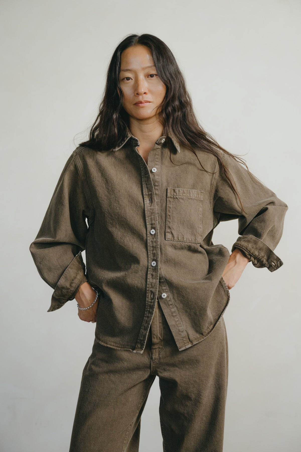 A woman modeling a matching brown corduroy button-up shirt and trousers set against a plain light gray studio background.