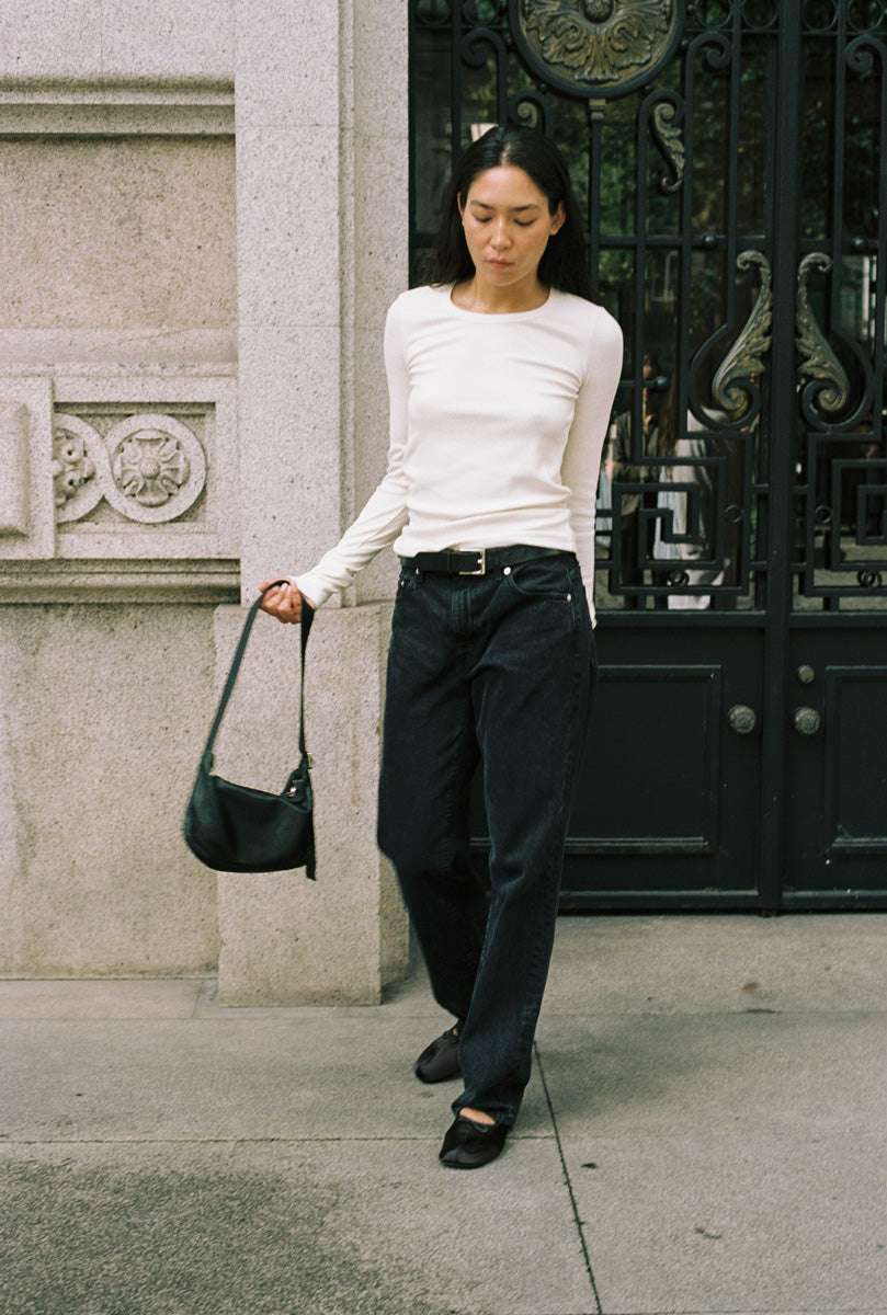 A woman standing in a doorway with a long sleeve tight white shirt and black jeans.